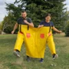 Zwei Personen laufen lachend gemeinsam in einer gelben Doppelhose über die Wiese, Team-Spiel mieten für Firmenanlässe und Feste